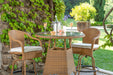 A Tortuga Outdoor Sea Pines 3-Piece Wicker Bar Set - Java or Mojave comprising of a wicker table and chairs in a garden.