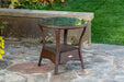 A Tortuga Outdoor Sea Pines Java side table with a glass top on a stone patio, showcasing all-weather resilience.