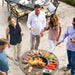 A social gathering around the Arteflame Classic 40" Grill, cooking various meats and vegetables.