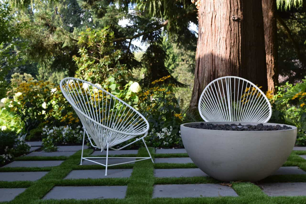  A tranquil garden scene featuring the Solus Decor Hemi Firebowl alongside modern outdoor seating, nestled amongst vibrant foliage and structured hardscaping.