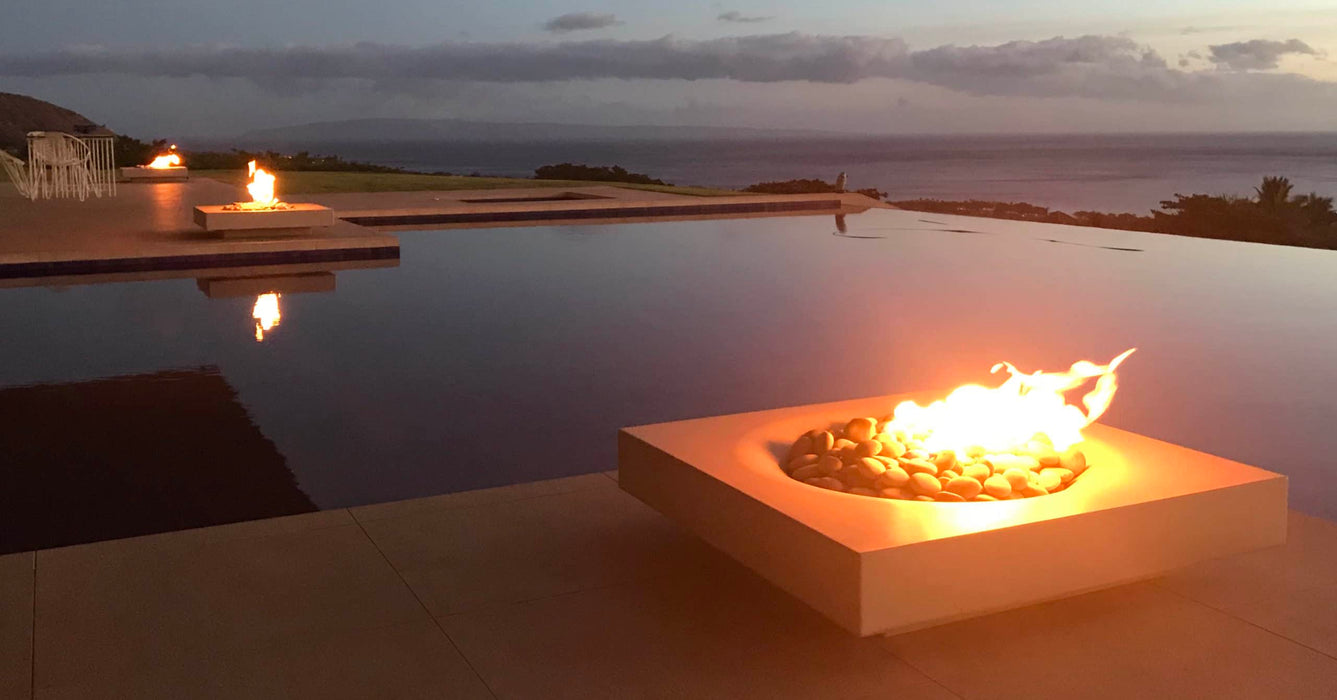The Solus Decor Halo Low Fire Pit radiates warmth by an infinity pool as twilight descends, creating a serene and inviting outdoor ambiance.