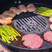 Gourmet cooking scene with an Arteflame grill grate insert on a Weber, showcasing burgers and asparagus prepared al fresco.
