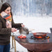 A person cooking seafood on the Arteflame Classic 40" Grill during winter, highlighting its all-season use.