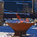A snowy scene where an Arteflame 40 inch fire pit with a low euro base stands ablaze, contrasting the cold with its warm, inviting flames.