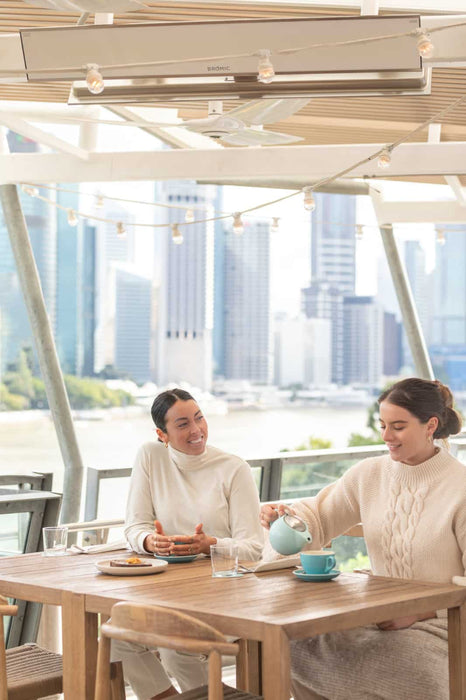 Outdoor alfresco restaurant in Brisbane featuring the Bromic Heating Platinum Smart-Heat 3400w electric patio heater, with urban buildings in the backdrop, offering a warm welcome.