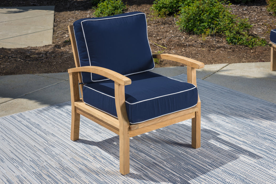 A Tortuga Outdoor 5-Piece Indonesian Teak Loveseat and Fire Table Set - Canvas Natural or Navy with a blue cushion on a rug, creating a luxury retreat.
