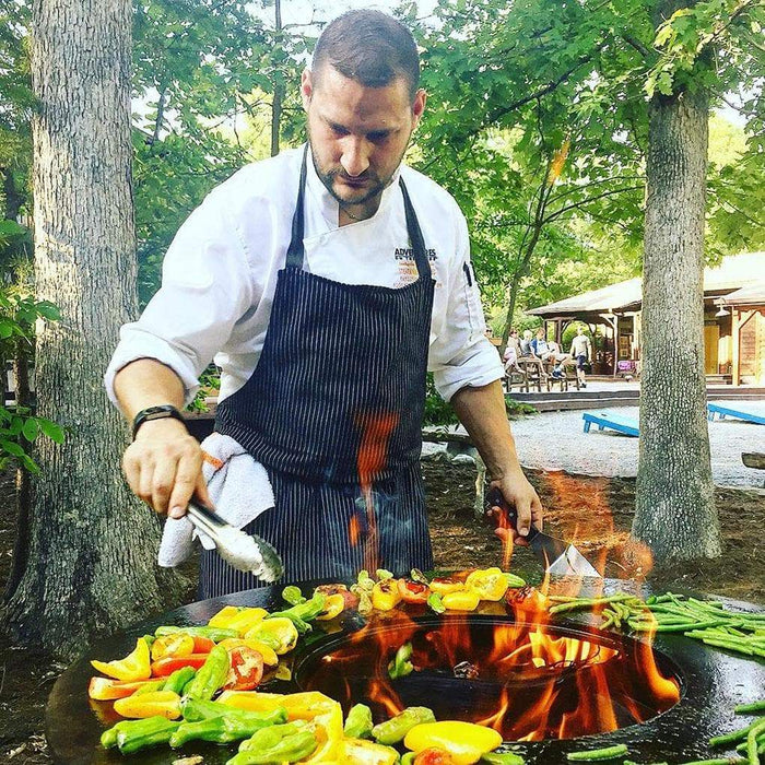 Professional chef preparing colorful vegetables on the Arteflame 20 inch grill in an outdoor setting.
