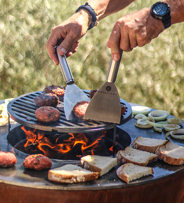 Action shot of cooking burgers on the Arteflame 20 inch grill, highlighting the grill's versatility.