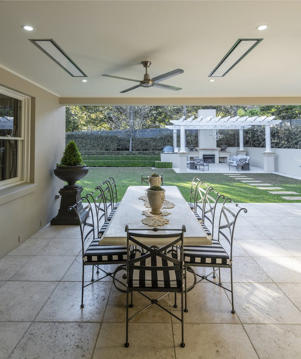 Elegant residential outdoor dining space with Bromic Platinum electric heaters integrated into the ceiling, complementing the sophisticated decor and green garden backdrop.