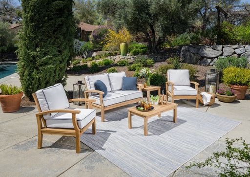 A durable construction Tortuga Outdoor 5-Piece Indonesian Teak Loveseat Set with Sunbrella Canvas Natural or Navy cushions and a blue rug.