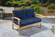 A Tortuga Outdoor teak outdoor loveseat with navy cushions on a durable construction.