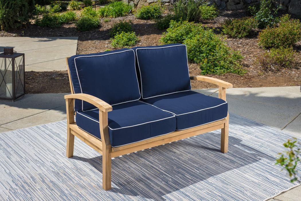 This Tortuga Outdoor 5-Piece Indonesian Teak Loveseat Set - Sunbrella Canvas Natural or Navy features a teak outdoor loveseat with blue cushions on a rug. The durable construction ensures longevity of this Tortuga Outdoor wicker furniture set.