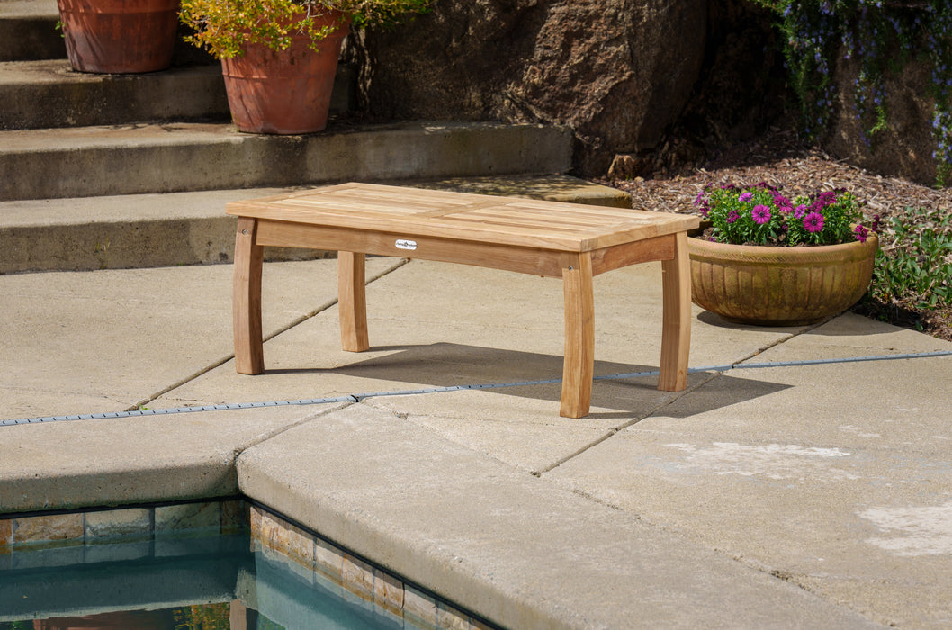 A durable Tortuga Outdoor wooden bench next to a pool.