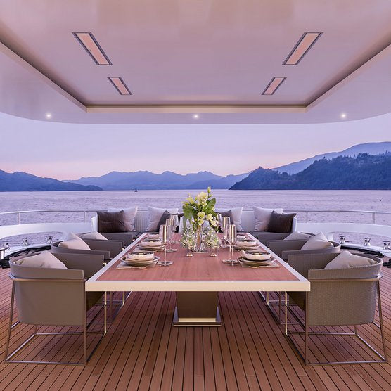 Luxurious yacht dining area with Bromic Platinum 2300w electric heaters installed overhead, offering warmth and comfort against the scenic backdrop of a serene mountainous shoreline at dusk.